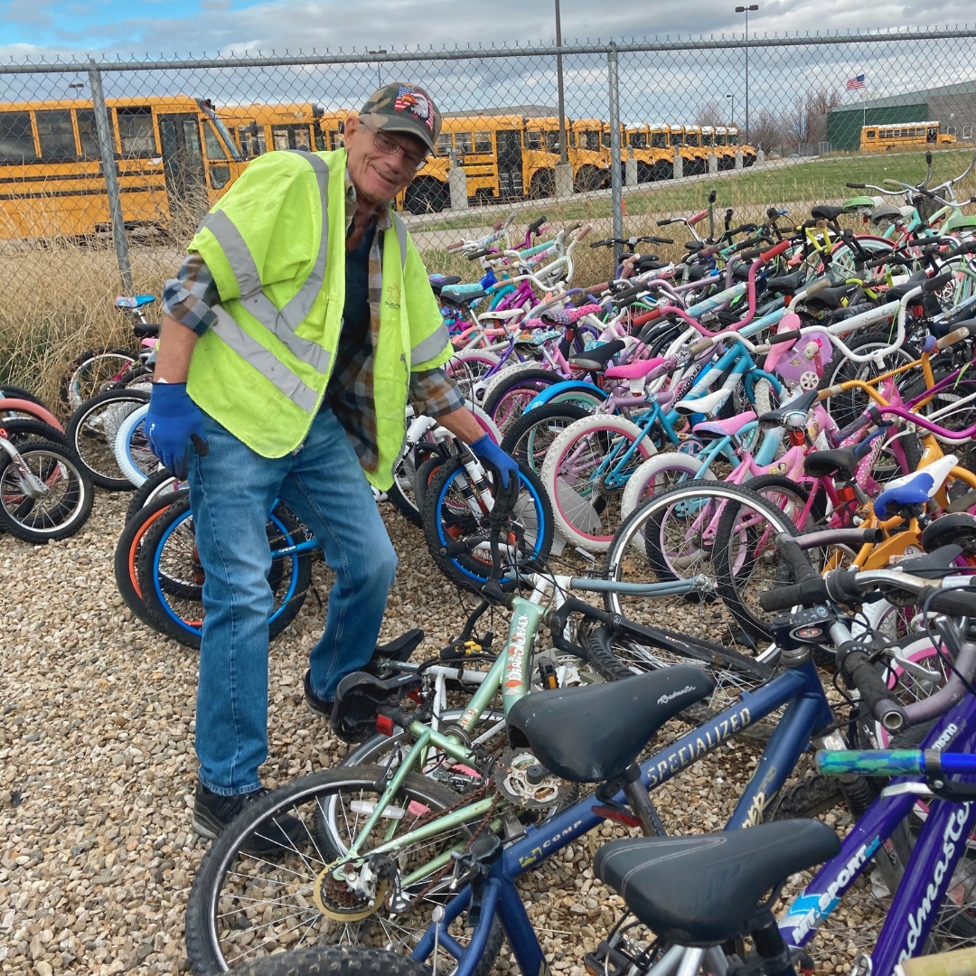 Long-time volunteer posing with hundreds of bikes that he fixed for the Recycle a Bicycle program